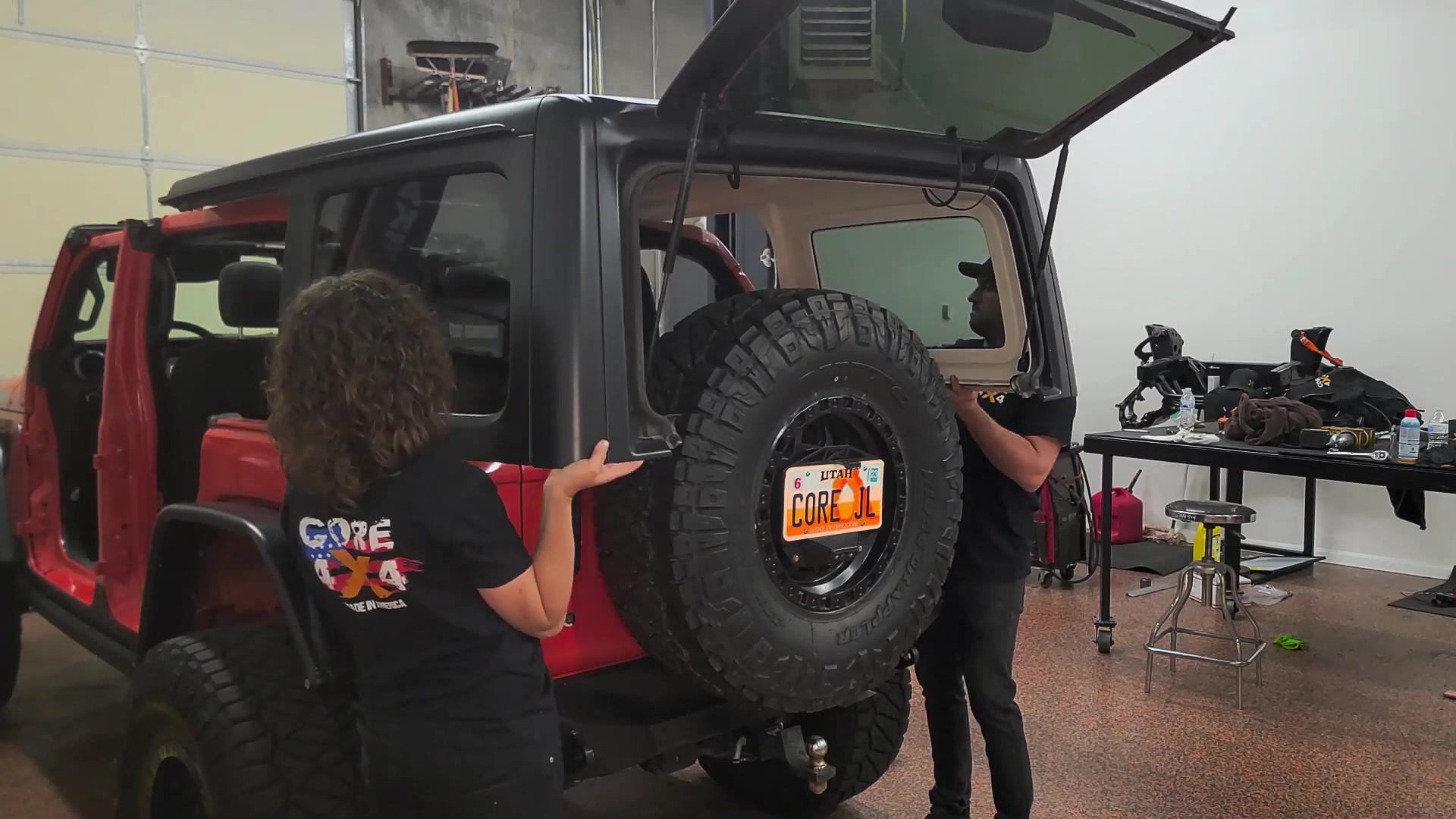 Spence and Marissa lifting the hardtop off the red Jeep JL Wrangler together in the shop