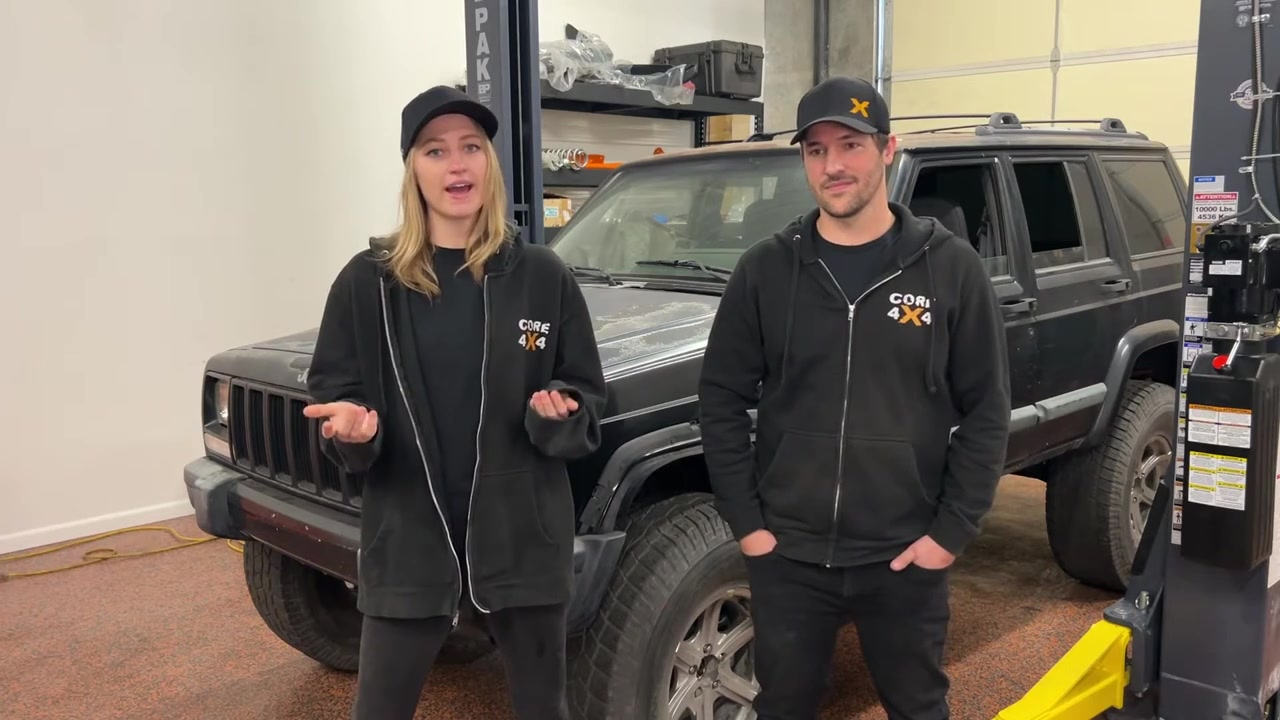 Gabby explaining the XJ off-road prep checklist with the Cherokee visible behind her in the Core 4x4 shop