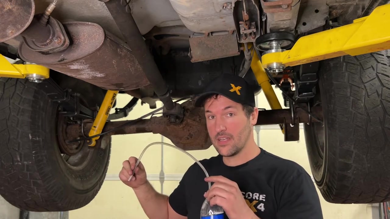 Spence underneath the XJ Cherokee showing the makeshift brake bleeder kit with clear hose and catch bottle