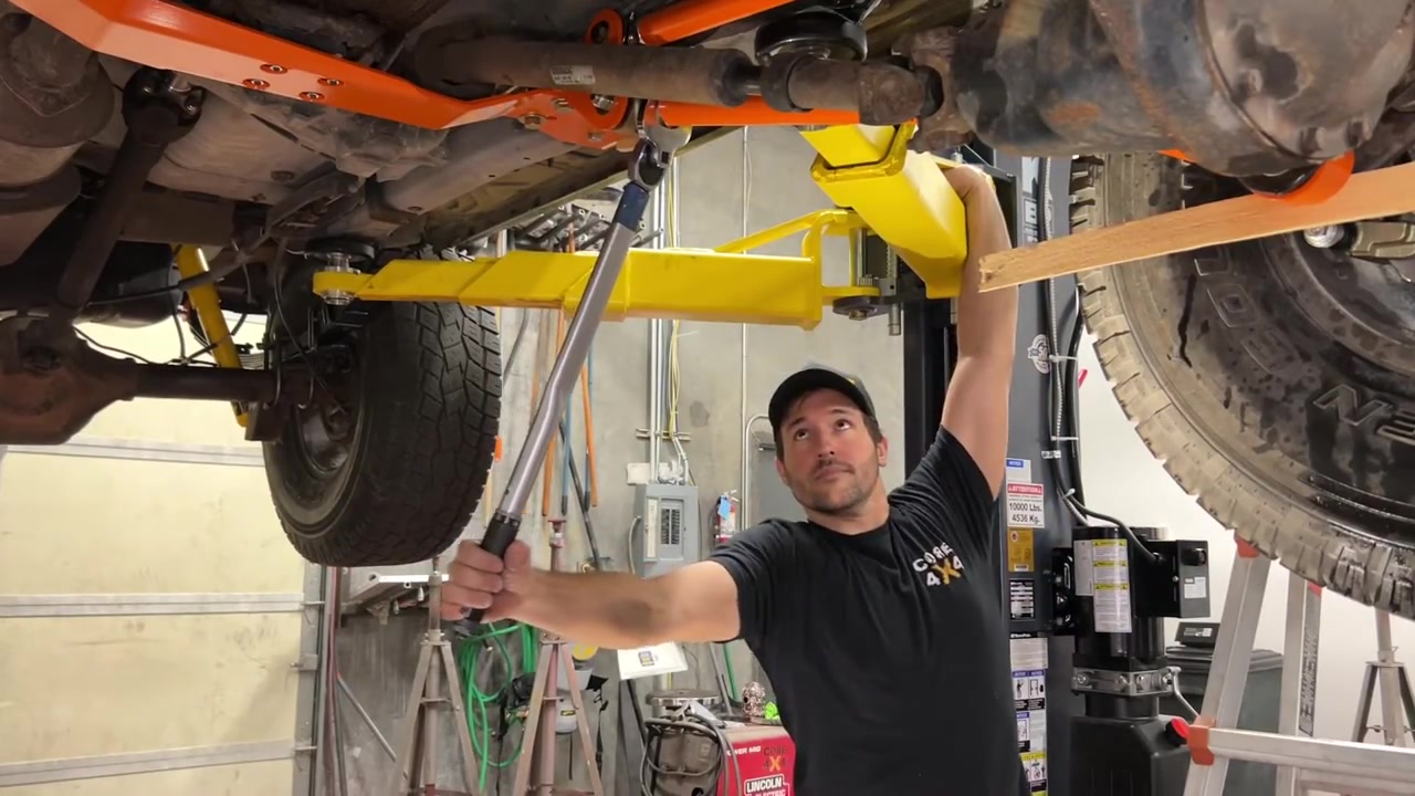 Spence using a torque wrench on the XJ suspension jam nuts underneath the lifted Cherokee with orange long arms visible