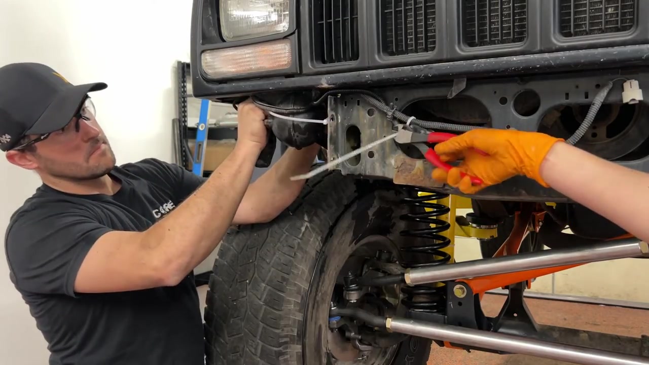 Spence and Gabby removing the front bumper from the XJ Cherokee showing the coil springs and long arm suspension behind