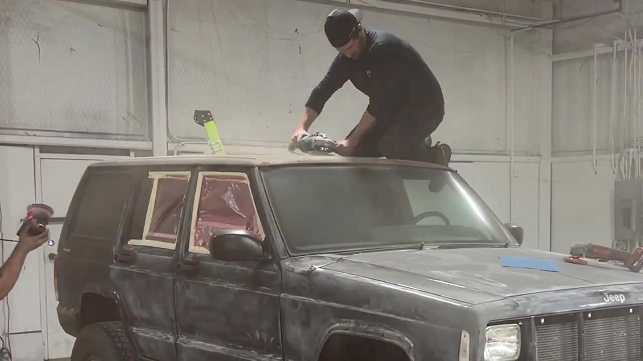 Spence on top of the XJ Cherokee sanding the roof with an orbital sander in preparation for Rhino lining