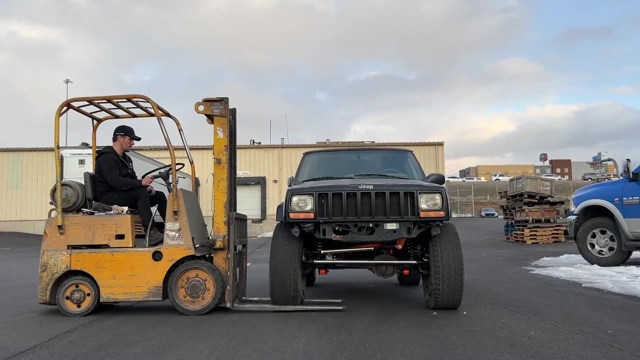 Spence using a forklift to flex test the XJ Cherokee outside the Core 4x4 shop with the front tire lifting off the ground