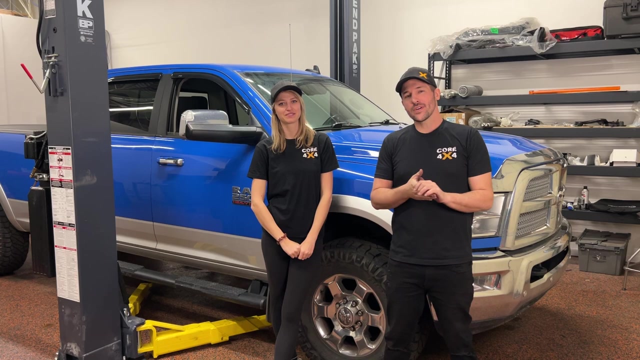 Gabby and Spence from Core 4x4 standing in front of the blue Ram 2500 in the shop before the rear control arm and track bar install
