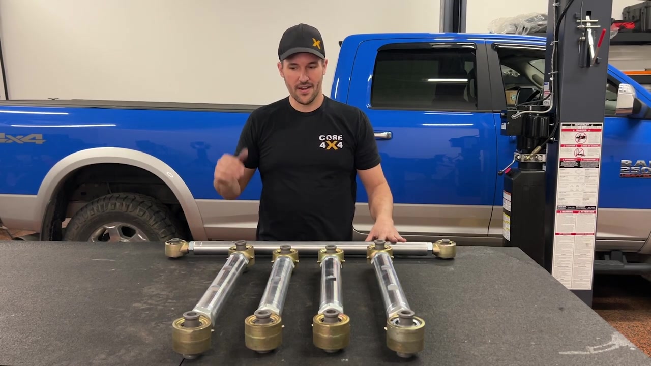 Spence at the workbench with the full Core 4x4 Aluminum Series rear control arm and track bar kit laid out for the Ram 2500, showing the 7075 aluminum construction and 3-inch Rock Jock Johnny Joints