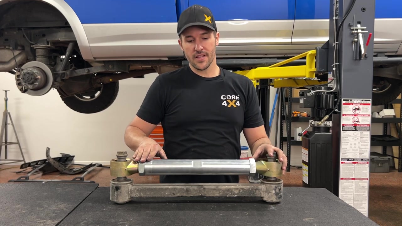 Spence holding the 3/4-ton aluminum series control arm on the workbench, showing the massive 3-inch Johnny Joint compared to the half-ton version