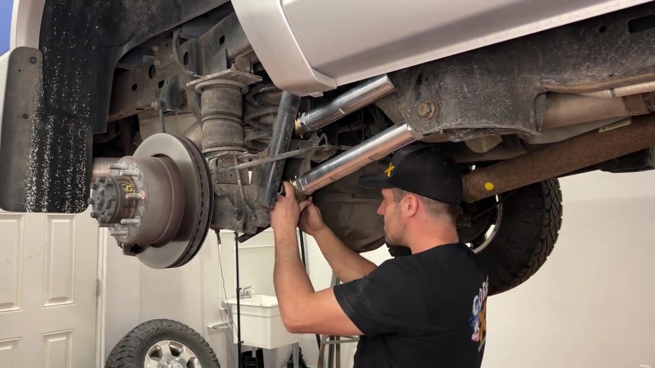 Spence under the Ram 2500 installing a new Core 4x4 Aluminum Series upper rear control arm, showing the one-arm-at-a-time method with the factory arms still in place