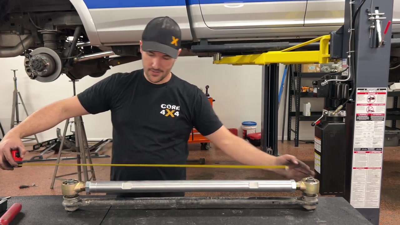 Spence at the workbench measuring the new Core 4x4 rear track bar for the Ram 2500, using a tape measure to set it to factory length