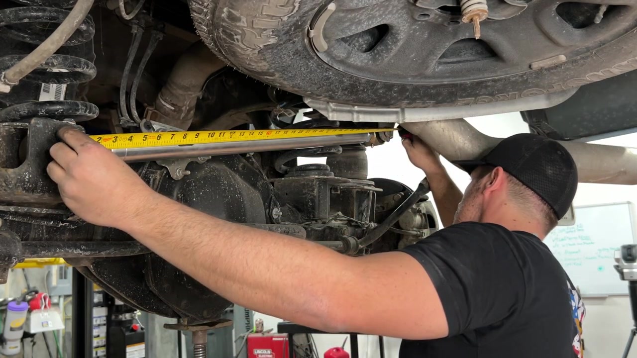 Spence measuring the installed track bar under the Ram 2500 using the outside-to-inside technique with a tape measure to verify the center-to-center length