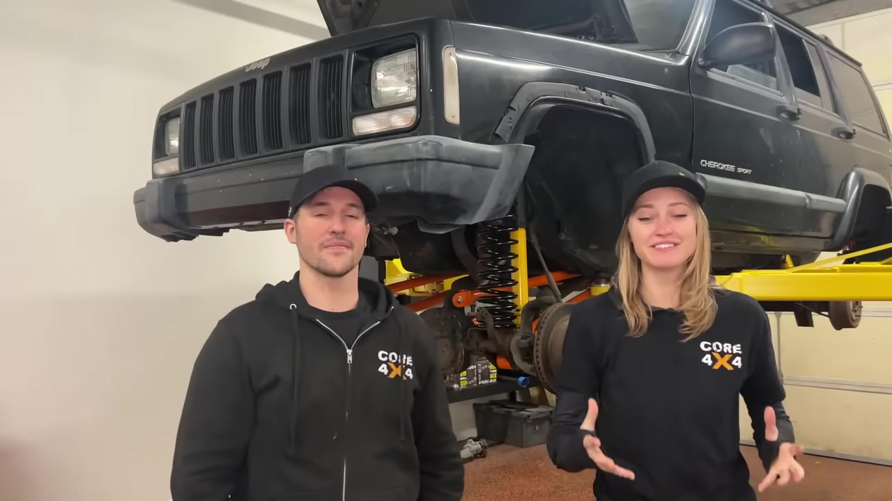 Spence and Gabby from Core 4x4 in front of a Jeep Cherokee XJ on the shop lift ready for the WJ knuckle swap