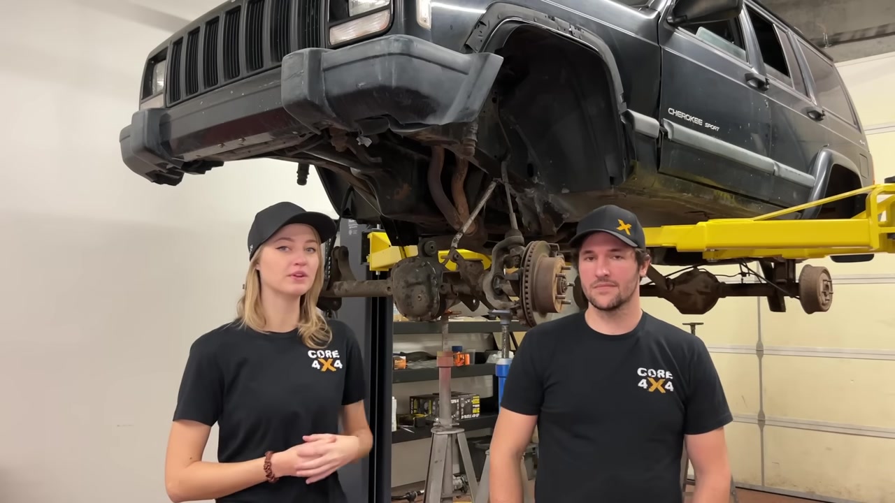 Gabby and Spence from Core 4x4 standing under the XJ Cherokee on the lift before the long arm kit install