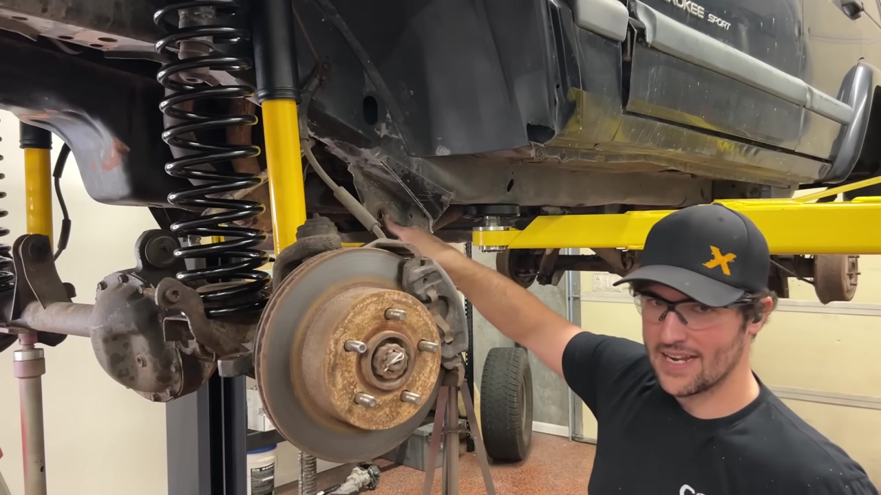 Spence pointing at the cut factory lower control arm bracket area on the XJ frame with new springs and shocks installed