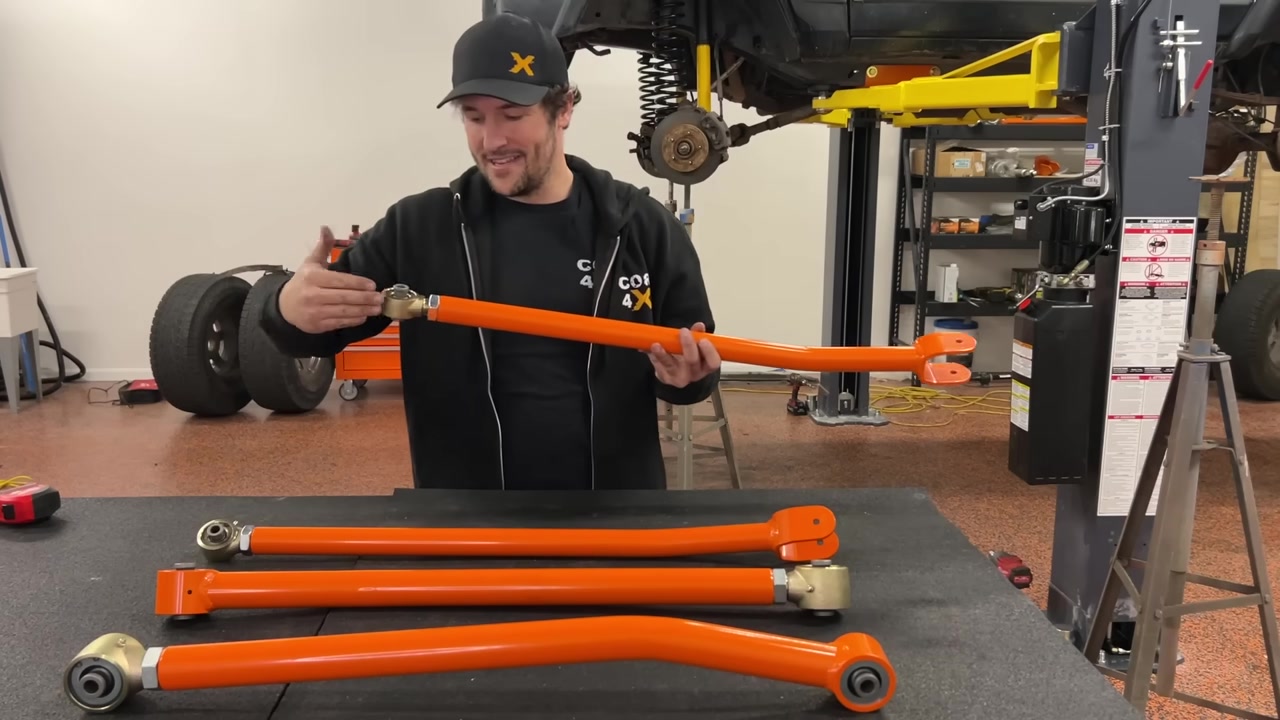 Spence holding orange Core 4x4 long arms with high-clearance bend laid out before installation on XJ Cherokee
