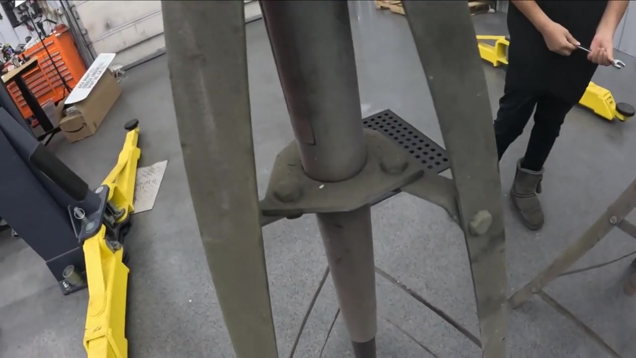 Close-up of old Harbor Freight jack stand covered in overspray and worn paint, with daughter using a wrench to disassemble it in the Core 4x4 shop