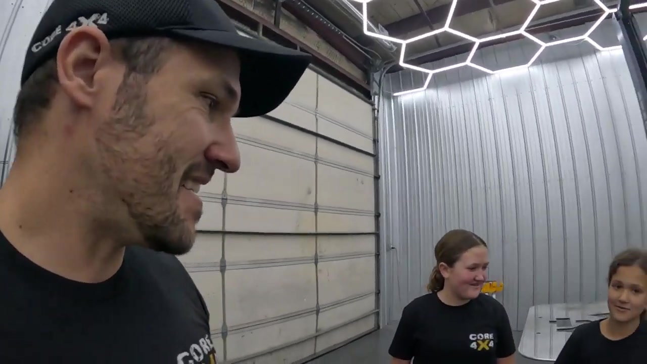 Spence smiling and talking with his daughters in the Core 4x4 shop during the jack stand reassembly project