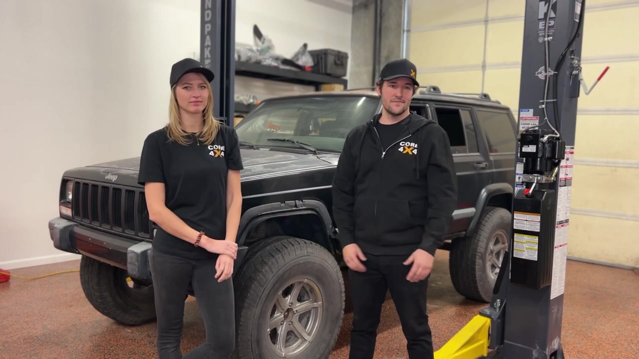 Spence and Gabby standing in front of the XJ Cherokee project vehicle at Core 4x4 shop