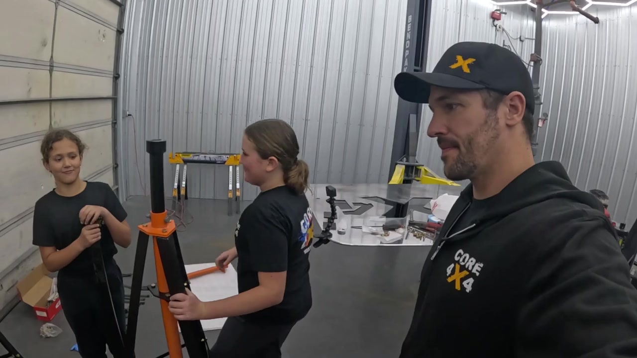 Both daughters assembling a freshly powder-coated orange and black jack stand in the Core 4x4 shop while Spence supervises