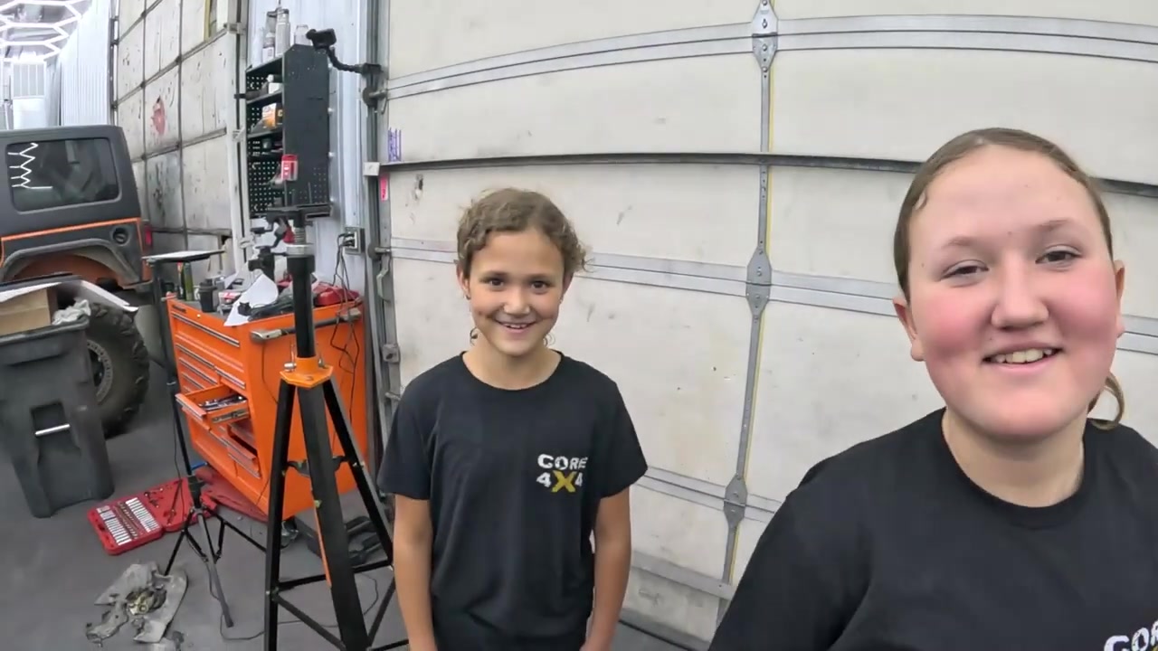 Spence's two daughters smiling in the Core 4x4 shop with the finished powder-coated jack stand visible behind them