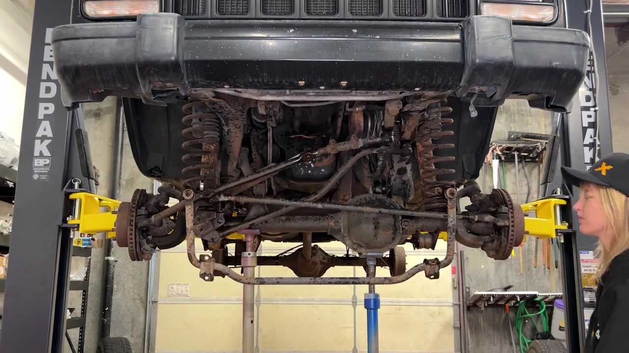 XJ Cherokee front end on the lift with steering and track bar removed, showing rusty undercarriage