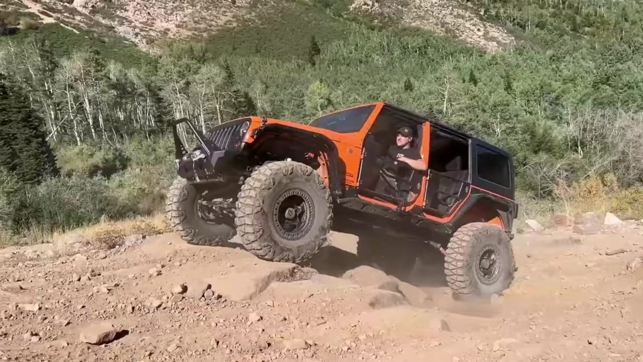 Orange Jeep JK navigating a steep off-road hill with large tires and Core 4x4 suspension components visible, demonstrating the suspension travel that requires proper bump stops