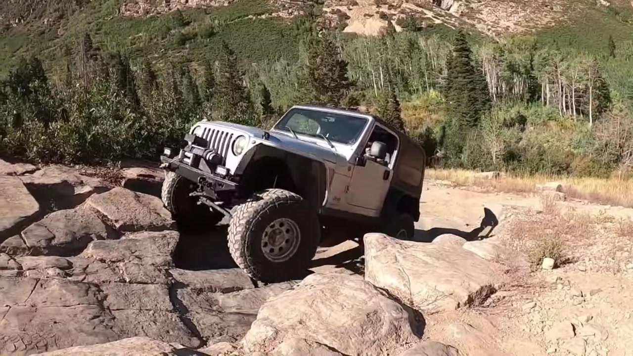 Silver Jeep JK crawling over rocky terrain on a mountain trail with suspension at full articulation, showing the importance of bump stops during off-road use
