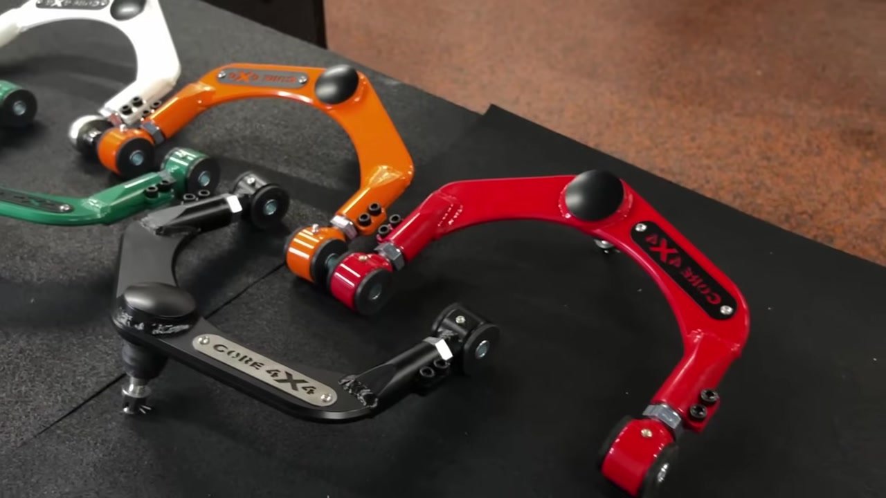 Core 4x4 Ram 1500 adjustable upper control arms displayed in multiple powder coat colors including black, green, orange, red, and white on the workbench