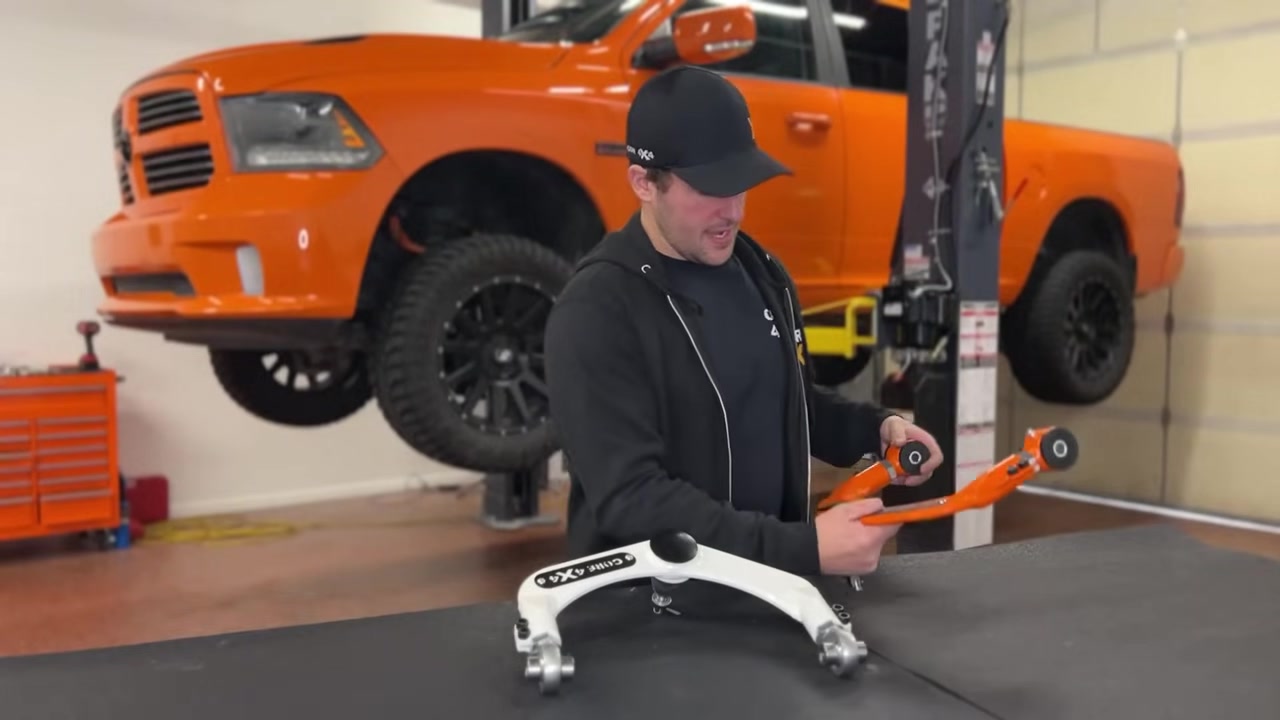 Spencer explaining the adjustability features of the Core 4x4 upper control arm, showing the adjustment sleeves on the factory arm and Core 4x4 arm side by side