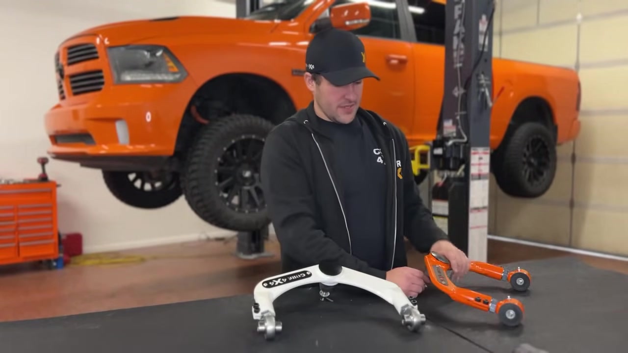 Spencer holding the factory white upper control arm showing the worn ball joint area, demonstrating why the non-replaceable joint is a problem on lifted trucks