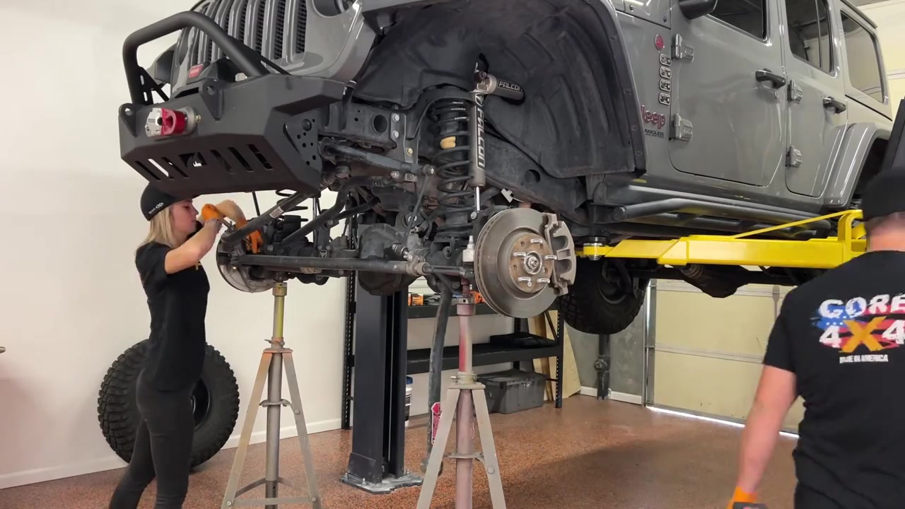 JL Wrangler on the lift with factory control arms removed and front axle exposed