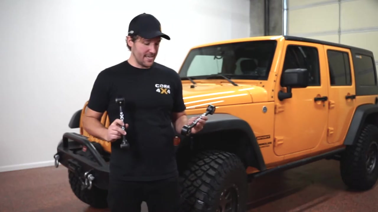 Spence from Core 4x4 holding crawler series front sway bar end links with Johnny Joints in front of an orange Jeep JK Wrangler Sport
