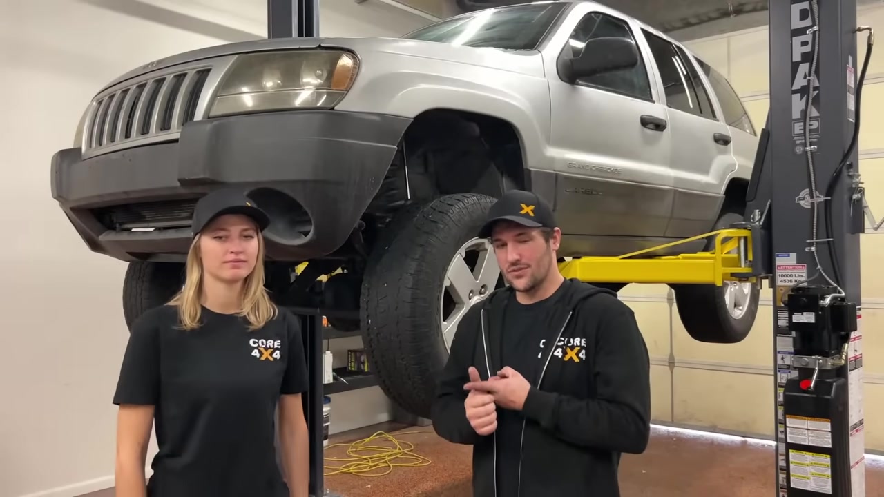 Spence explaining death wobble causes with WJ Grand Cherokee on the lift behind him
