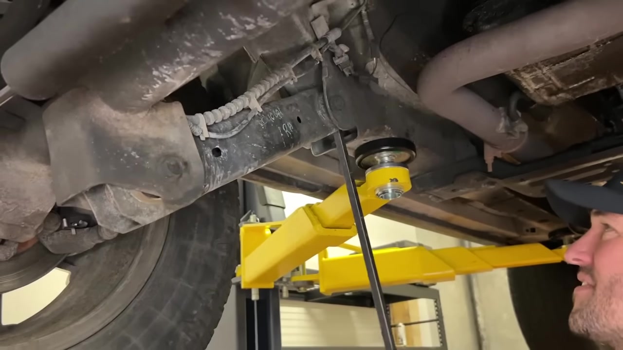 Checking control arm and track bar bushings under WJ Grand Cherokee with a pry bar on the lift