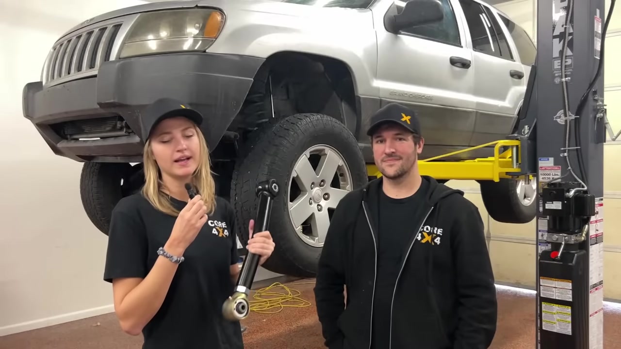 Gabby and Spence discussing the death wobble diagnosis with the WJ behind them, holding a new control arm