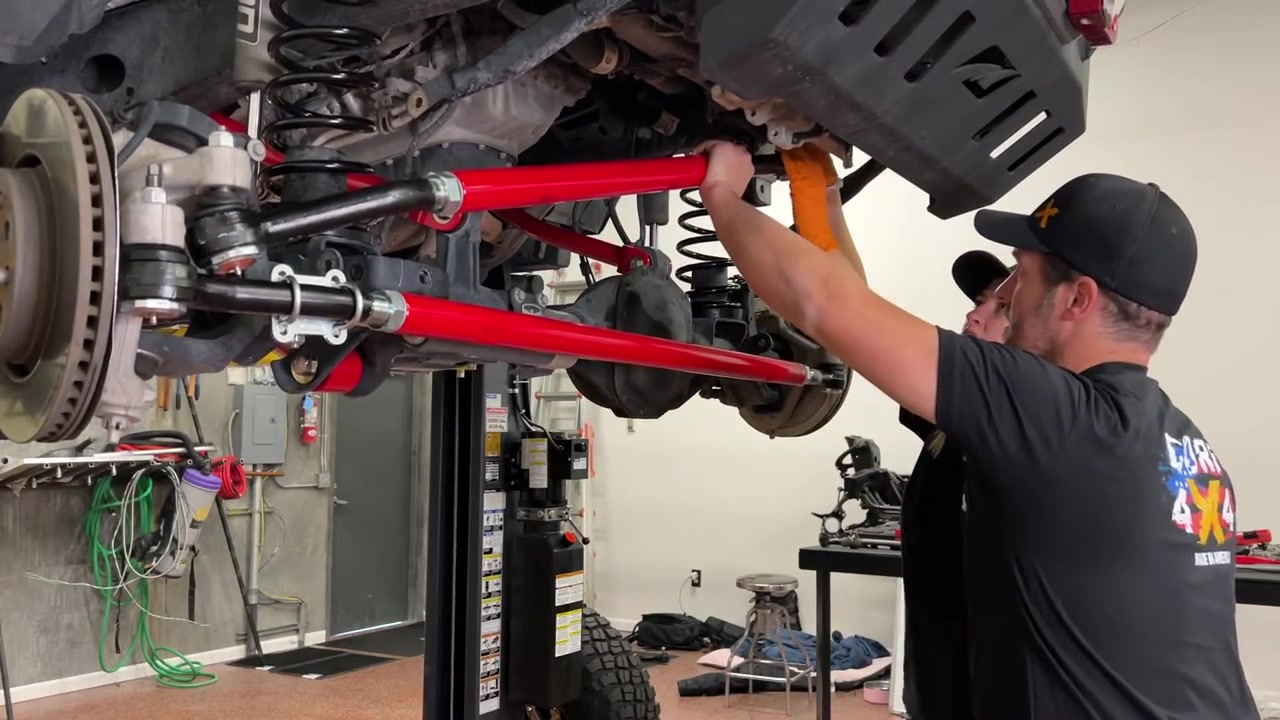 Spence under JL Wrangler installing front track bar with red Crawl Series components visible
