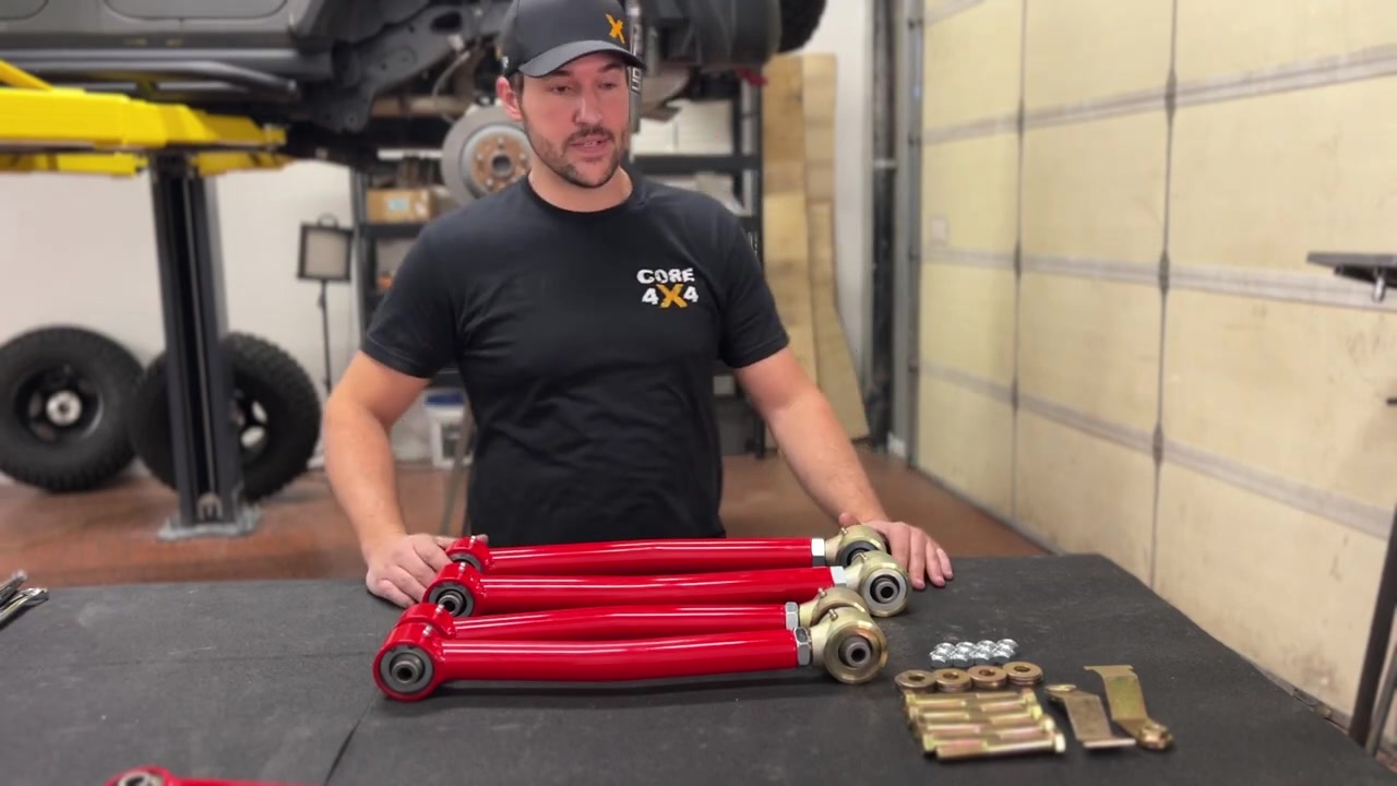 Spence at the workbench with the Crawl Series rear control arms laid out, showing the red powder-coated arms with Johnny Joints and the upgraded hardware kit beside them