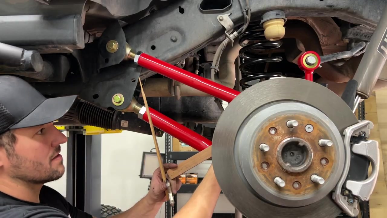 Spence under the JL Wrangler checking the newly installed red Crawl Series rear control arms near the rear axle with a tape measure to verify arm length