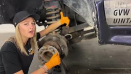 Gabby under the Dodge 3500 with the wheel removed, spraying penetrating oil on the old control arm bolts