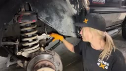 Gabby installing a new Core 4x4 Tier 4 control arm on the driver side of the Dodge 3500, working under the truck near the coil spring