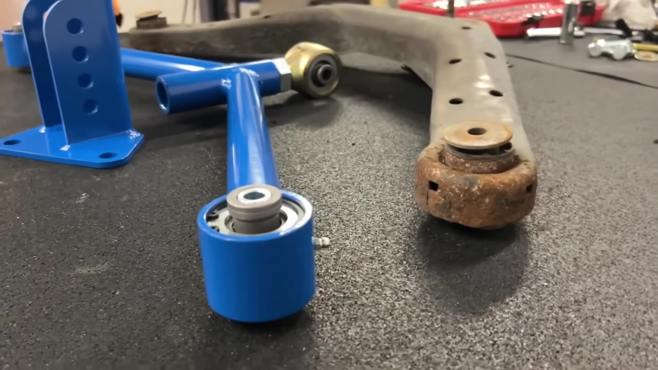 Core 4x4 Crawler Series rear upper A arm on the workbench next to the worn factory arm, showing the Johnny Joint vs the maxed-out factory ball joint