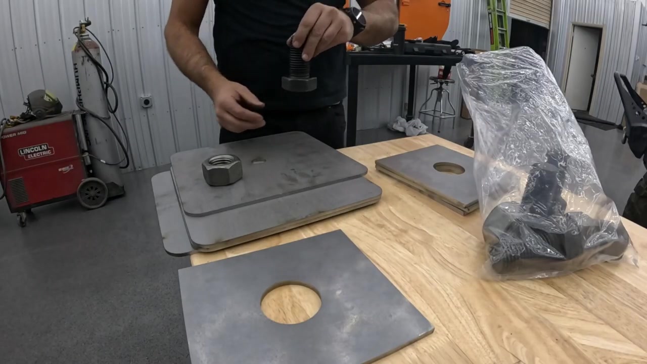 Laser-cut steel foot plates and mounting hardware laid out on a workbench with bolts and nuts for table leveling feet