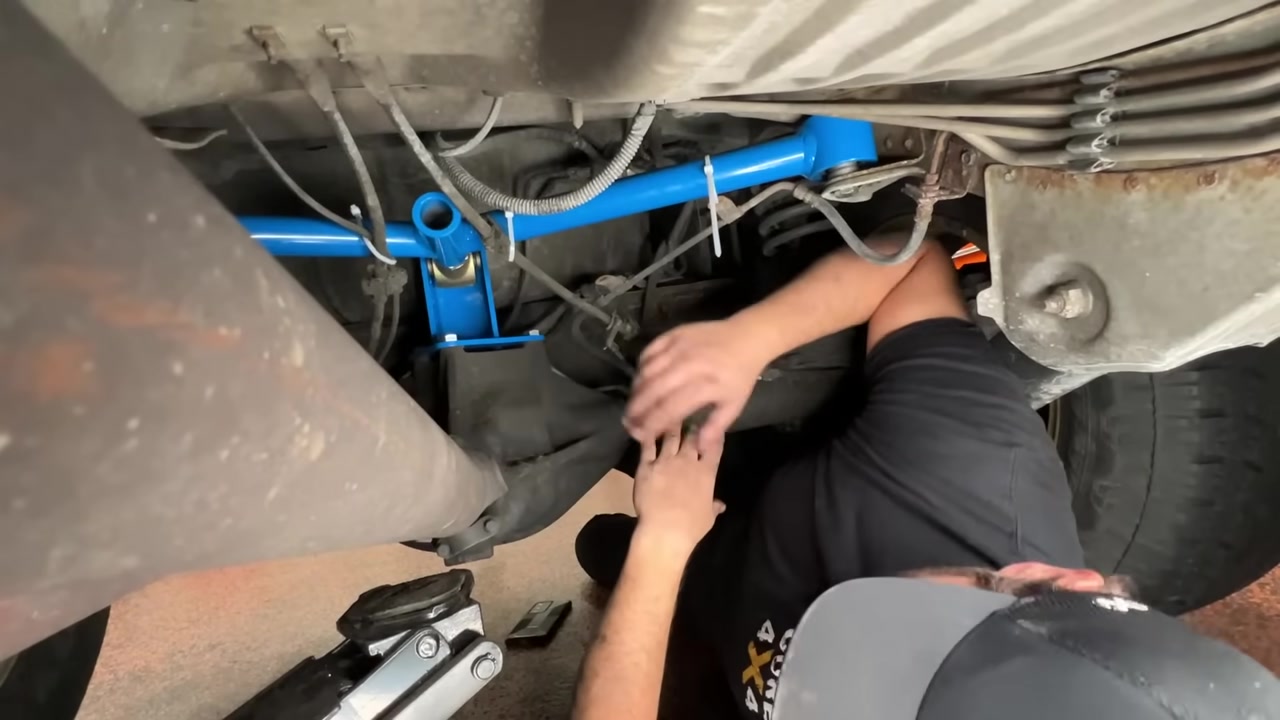 Spence setting the pinion angle and arm adjustment on the WJ Grand Cherokee with the Jeep lowered to the ground, showing the blue Crawler Series A arm and multi-hole bracket