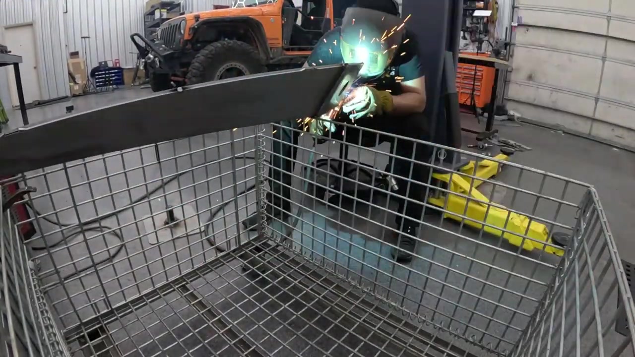 Welding sparks flying as the steel table base legs are being tacked together in the Core 4x4 fab shop with a Jeep visible in the background