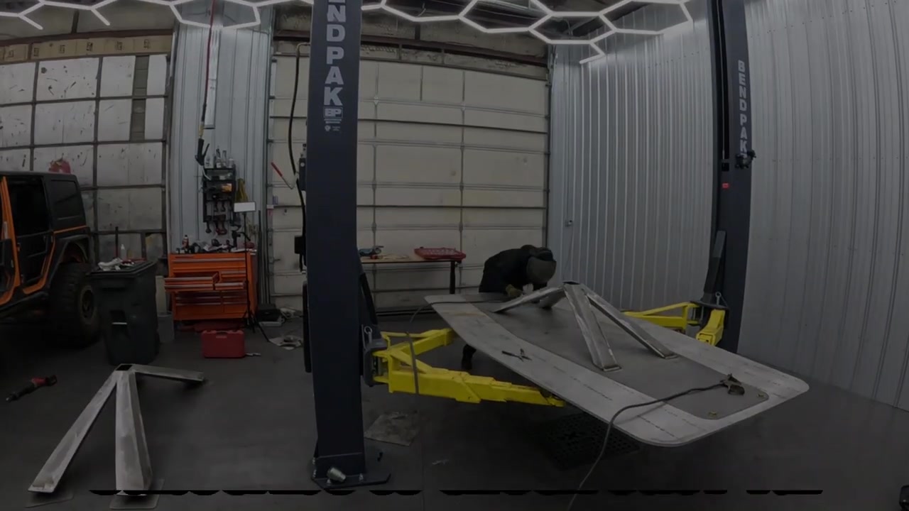 Wide shot of the Core 4x4 fab shop with the table base on the BendPak hoist and leg components visible on the shop floor