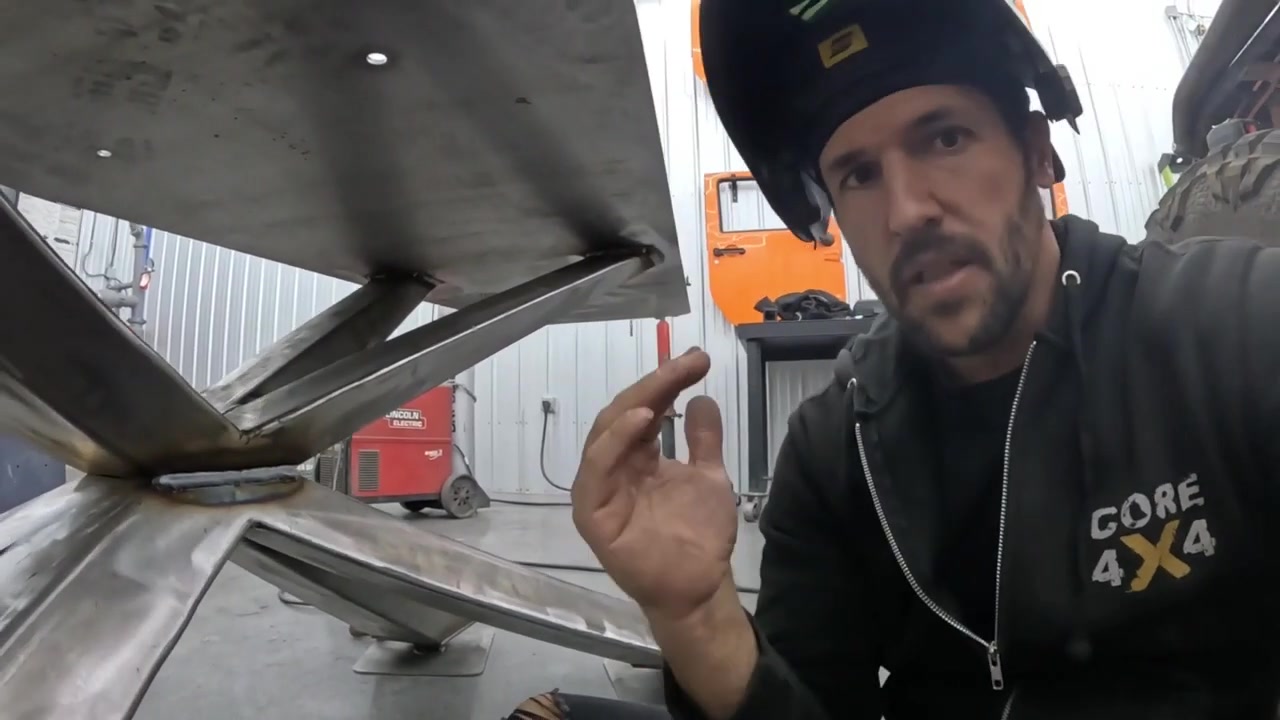 Spence with welding helmet showing the underside of the table base with legs and structural welds