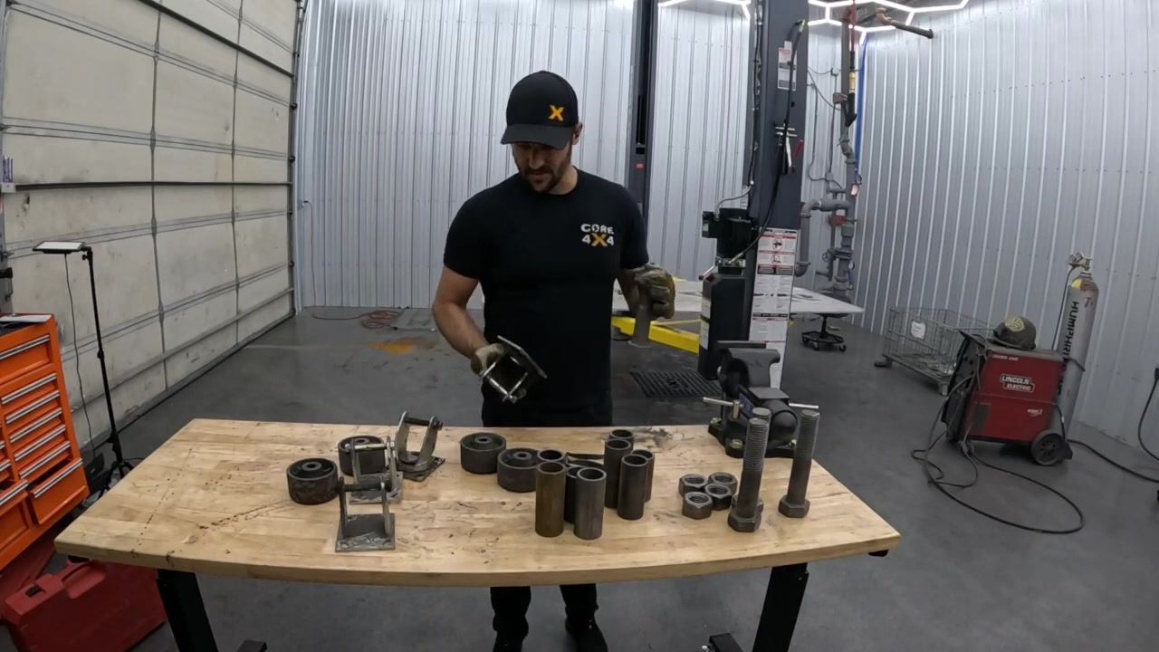 Spence building custom caster mounts and hardware at the workbench with welding supplies laid out