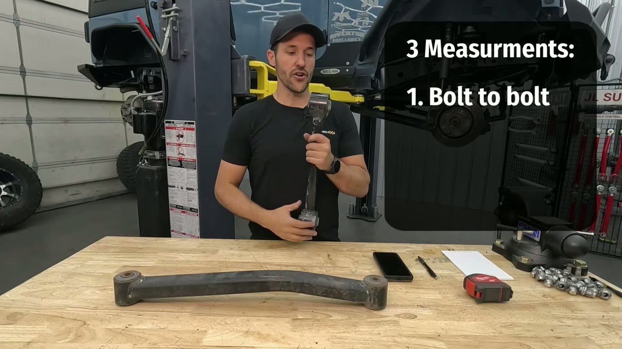 A control arm laid on the workbench with a tape measure and phone, alongside an on-screen note reading 3 Measurements, 1. Bolt to bolt