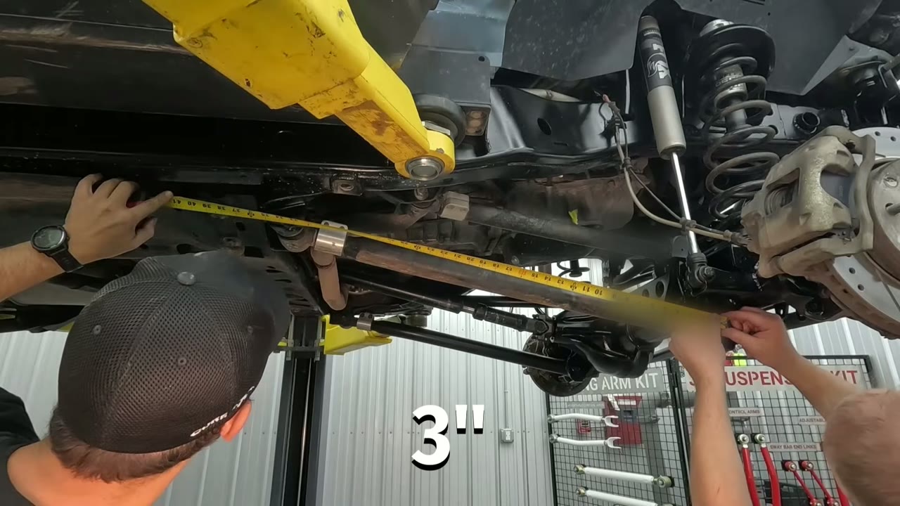 Measuring a control arm on the JKU with a tape measure while the Jeep is on the lift