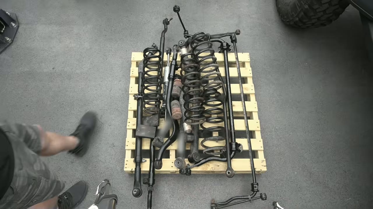 The old control arms, track bars, and coil springs removed from the Jeep laid out on a pallet